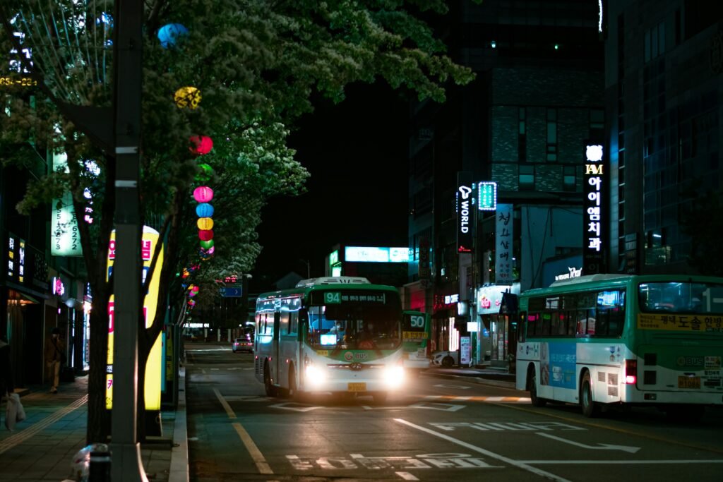 City street at night with buses, neon lights and urban traffic in illuminated downtown area